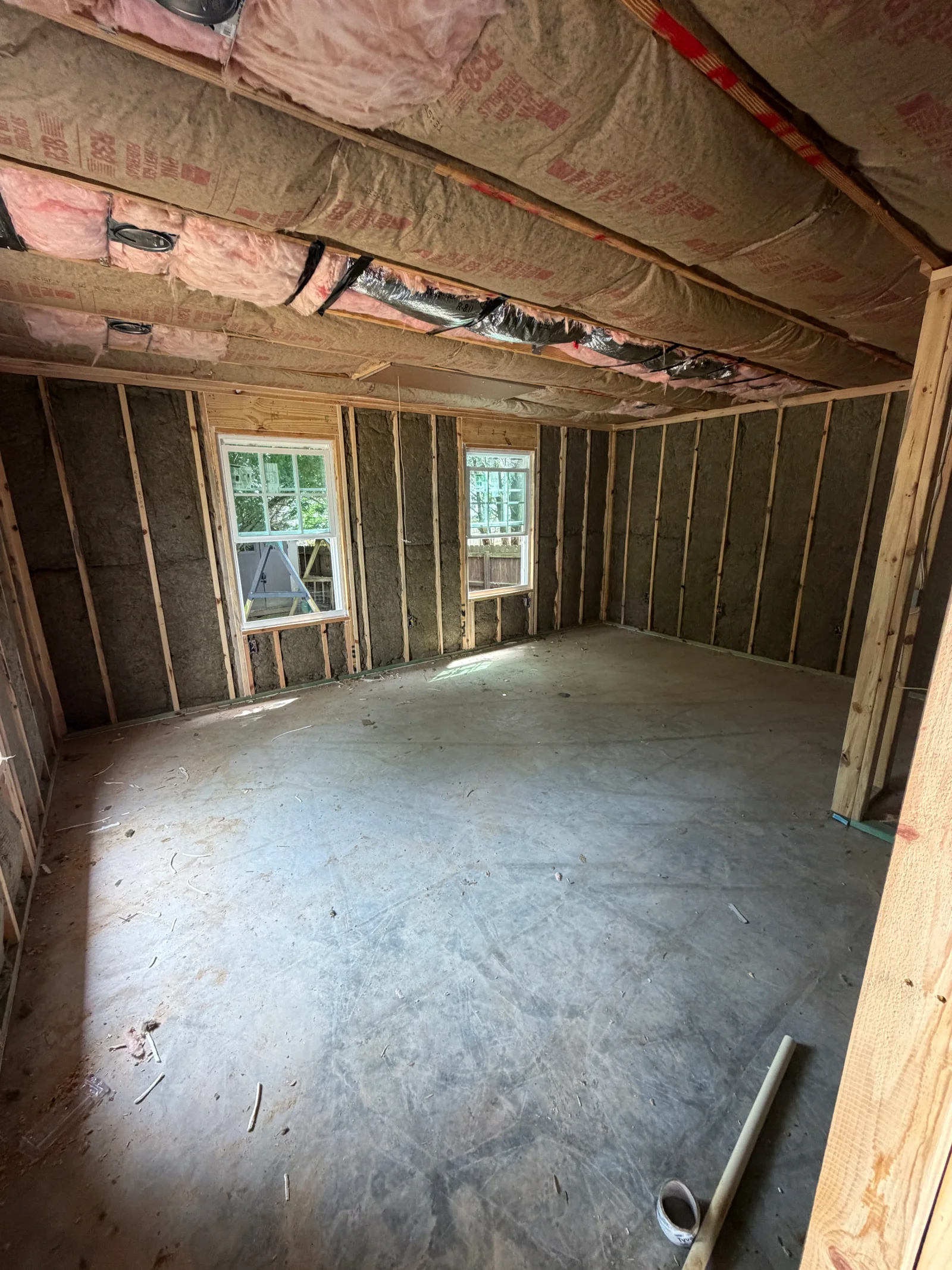Unfinished room with wood framing, fiberglass insulation in walls and ceiling, and two white vinyl windows