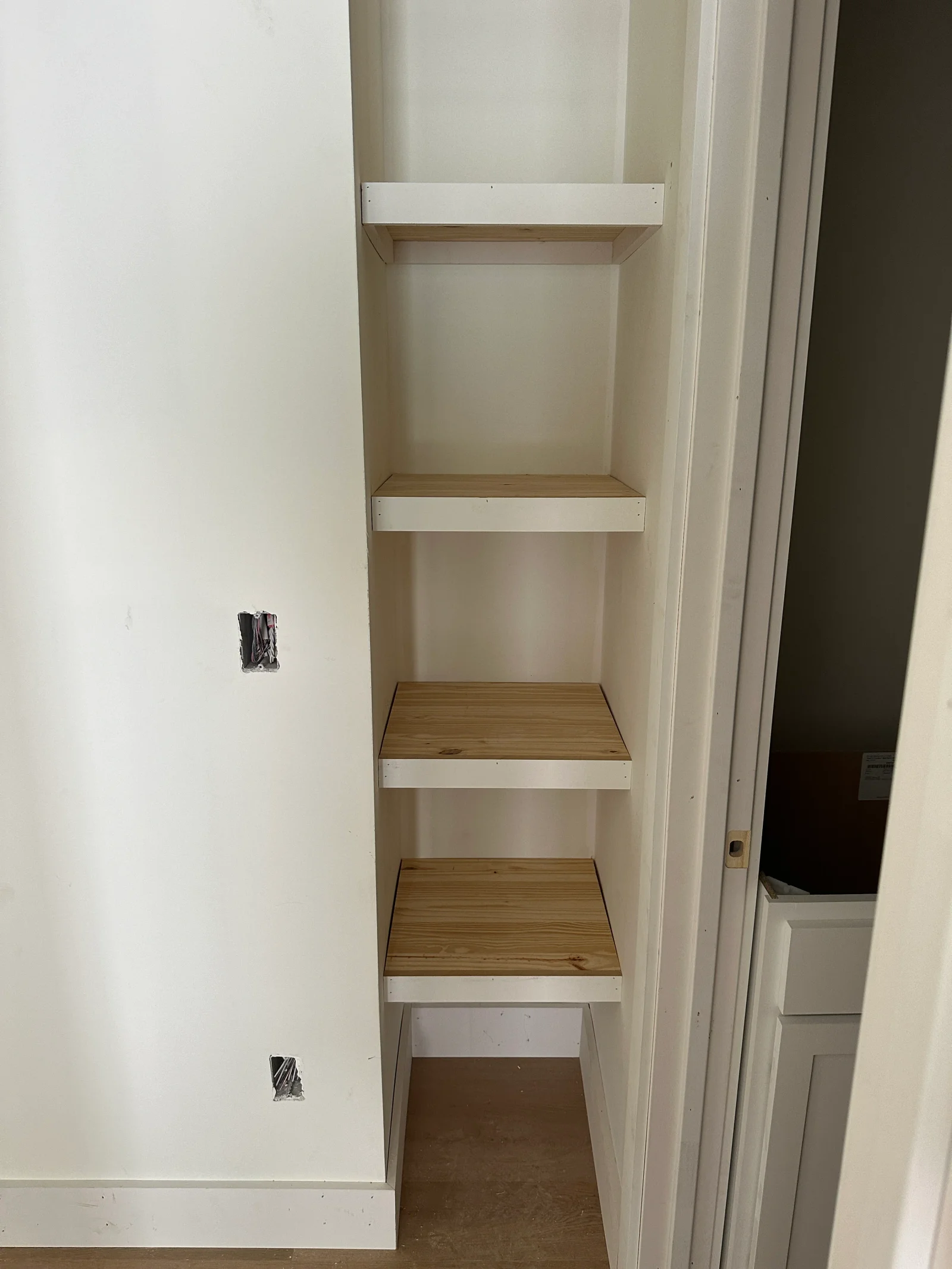 Built-in closet with four unfinished pine shelves and white-painted edge trim inside a narrow recess
