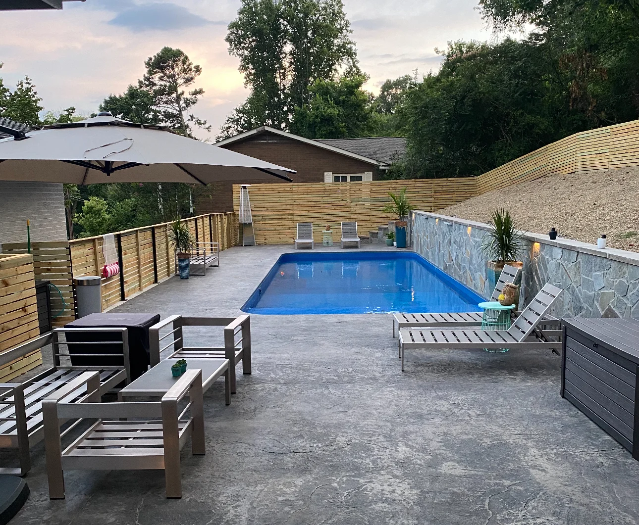 Stamped concrete pool deck with in-ground pool, horizontal wood privacy fence, stone retaining wall, and aluminum patio furniture