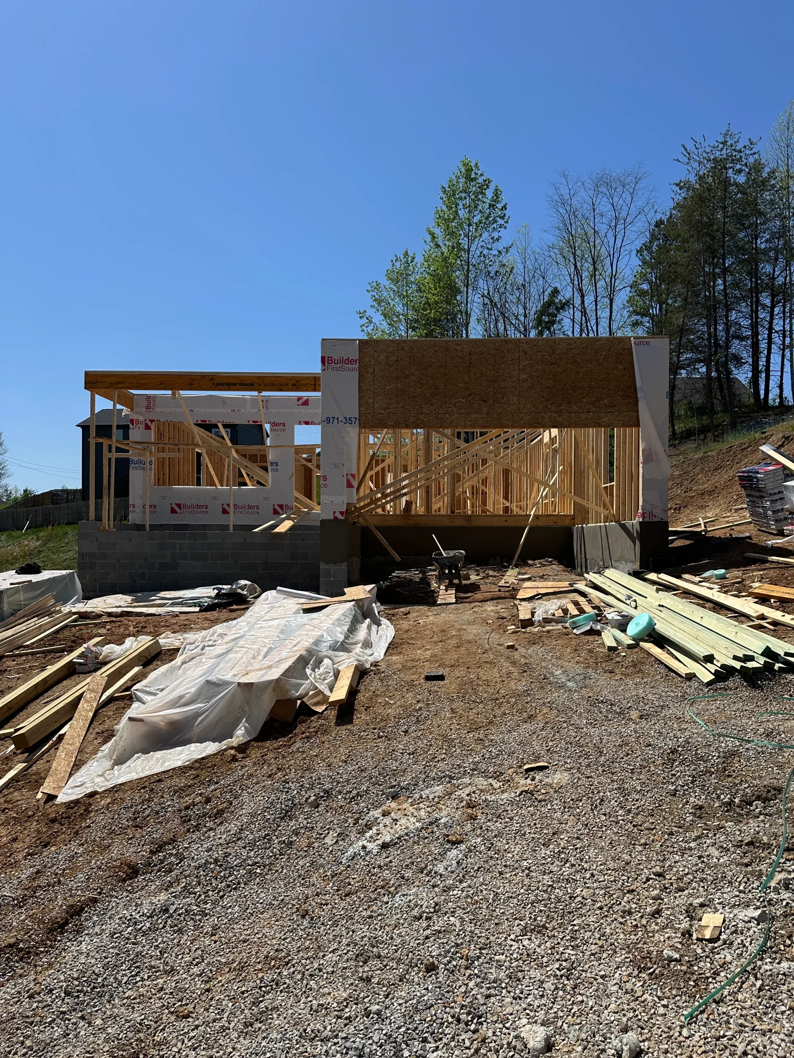 New home framing with OSB wall sheathing, housewrap, engineered roof trusses, and concrete block foundation wall