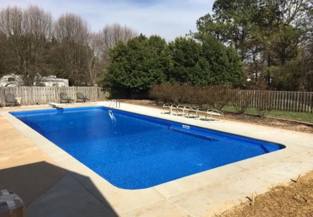 Rectangular in-ground pool with blue liner, concrete deck, stainless steel ladder, and diving board