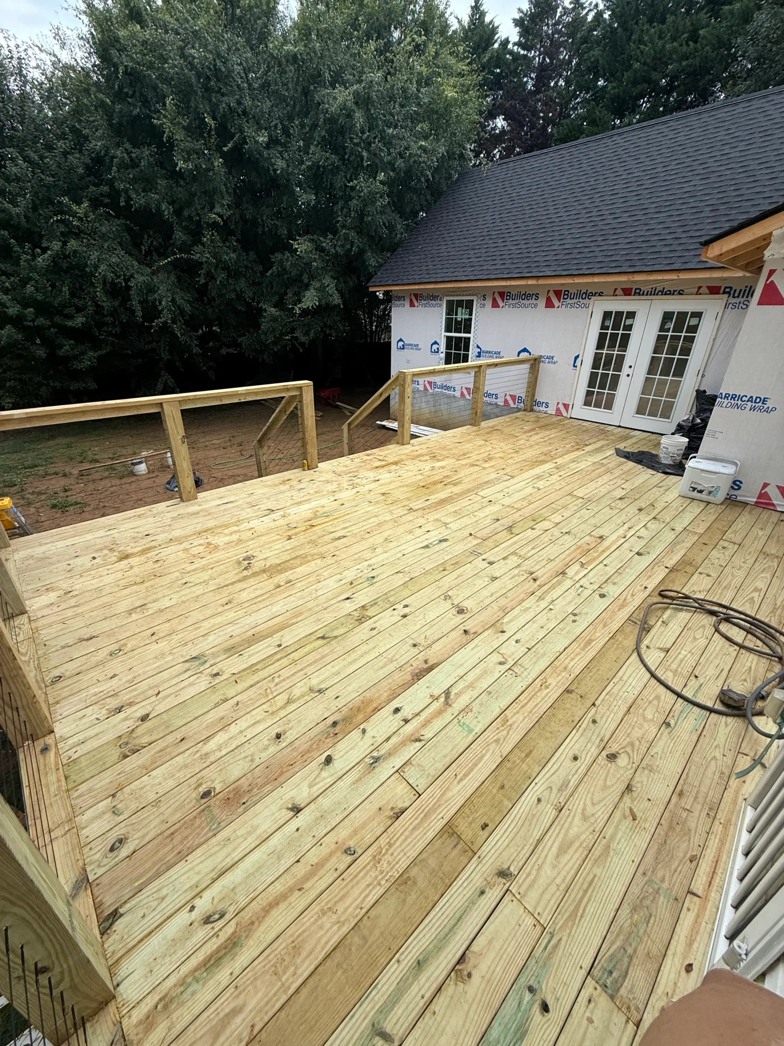 Pressure-treated wood deck with horizontal cable railing and wood posts beside white French doors