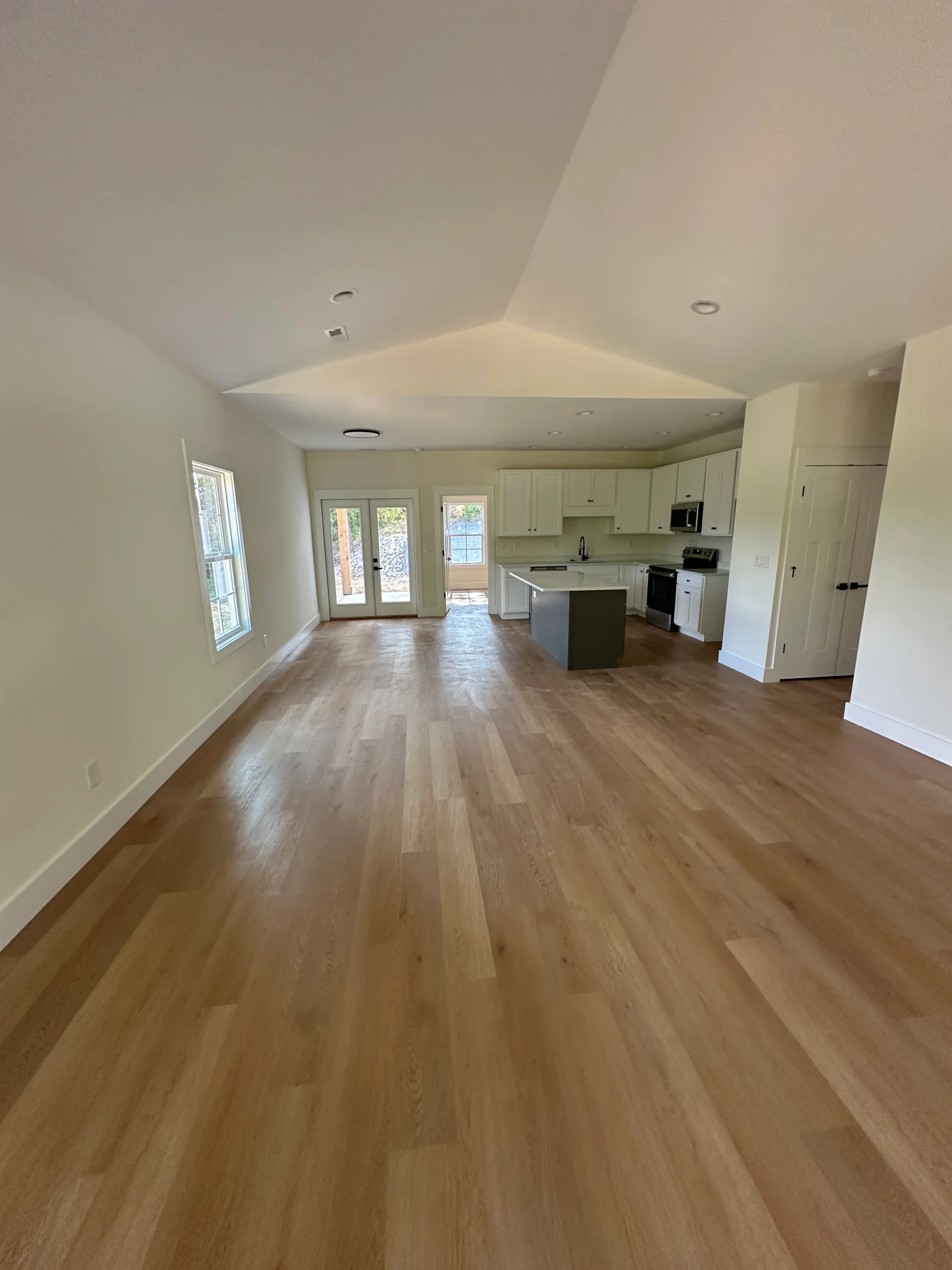Open living and kitchen with vaulted ceiling, wood-look vinyl plank floors, white shaker cabinets, and gray island