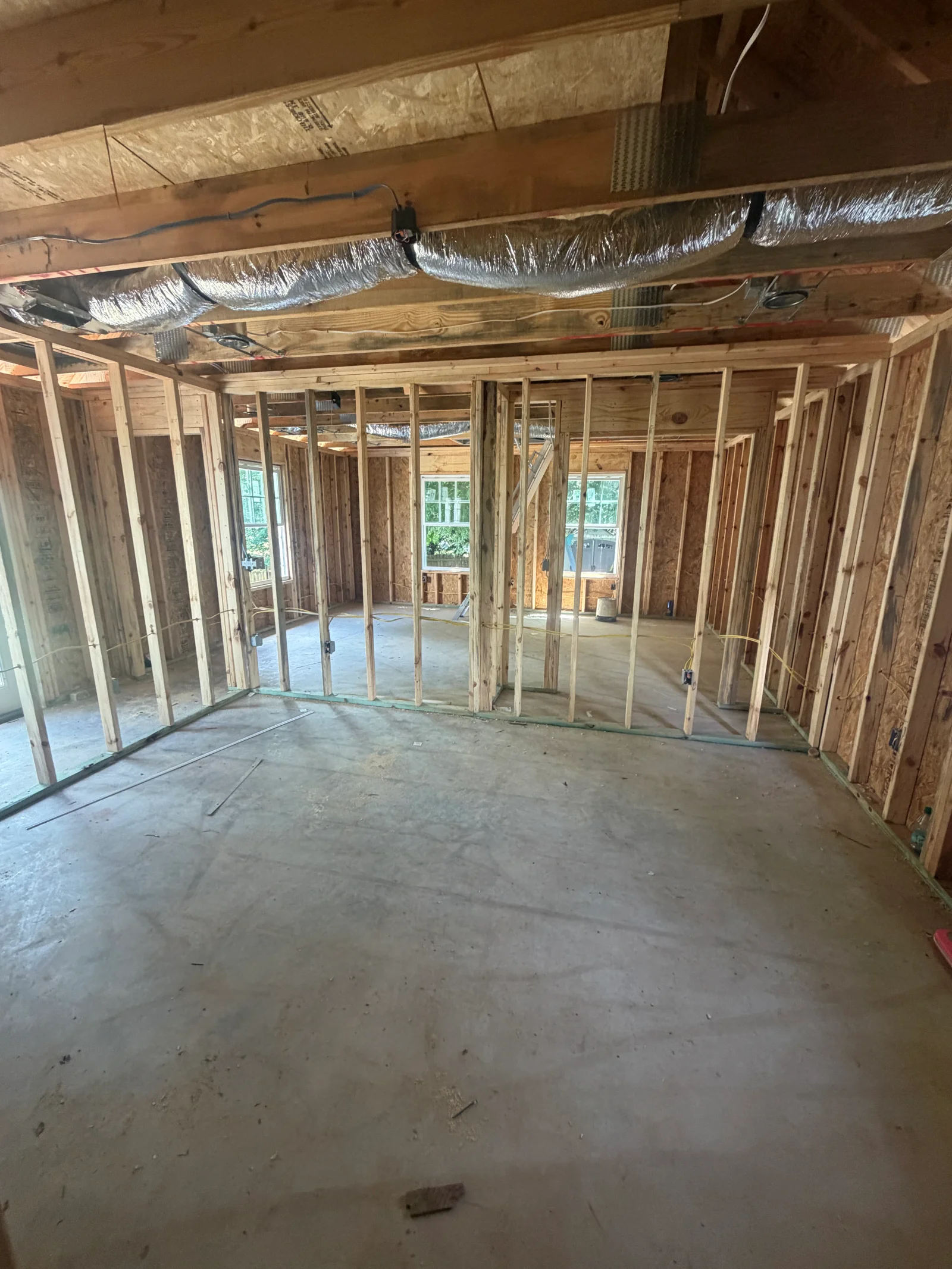 Open wood-framed interior with exposed studs, OSB sheathing, silver flex ductwork, and wiring at rough-in stage