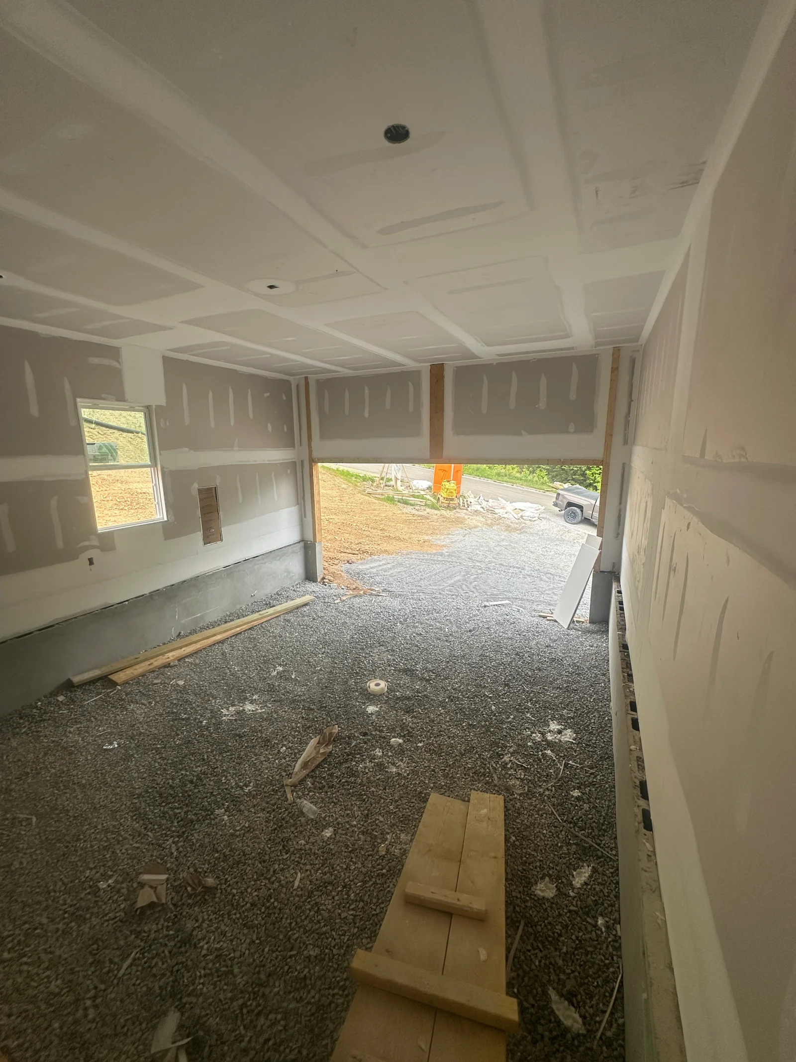 Interior room with taped and mudded drywall, coffered ceiling, window, gravel floor, and open bay to exterior