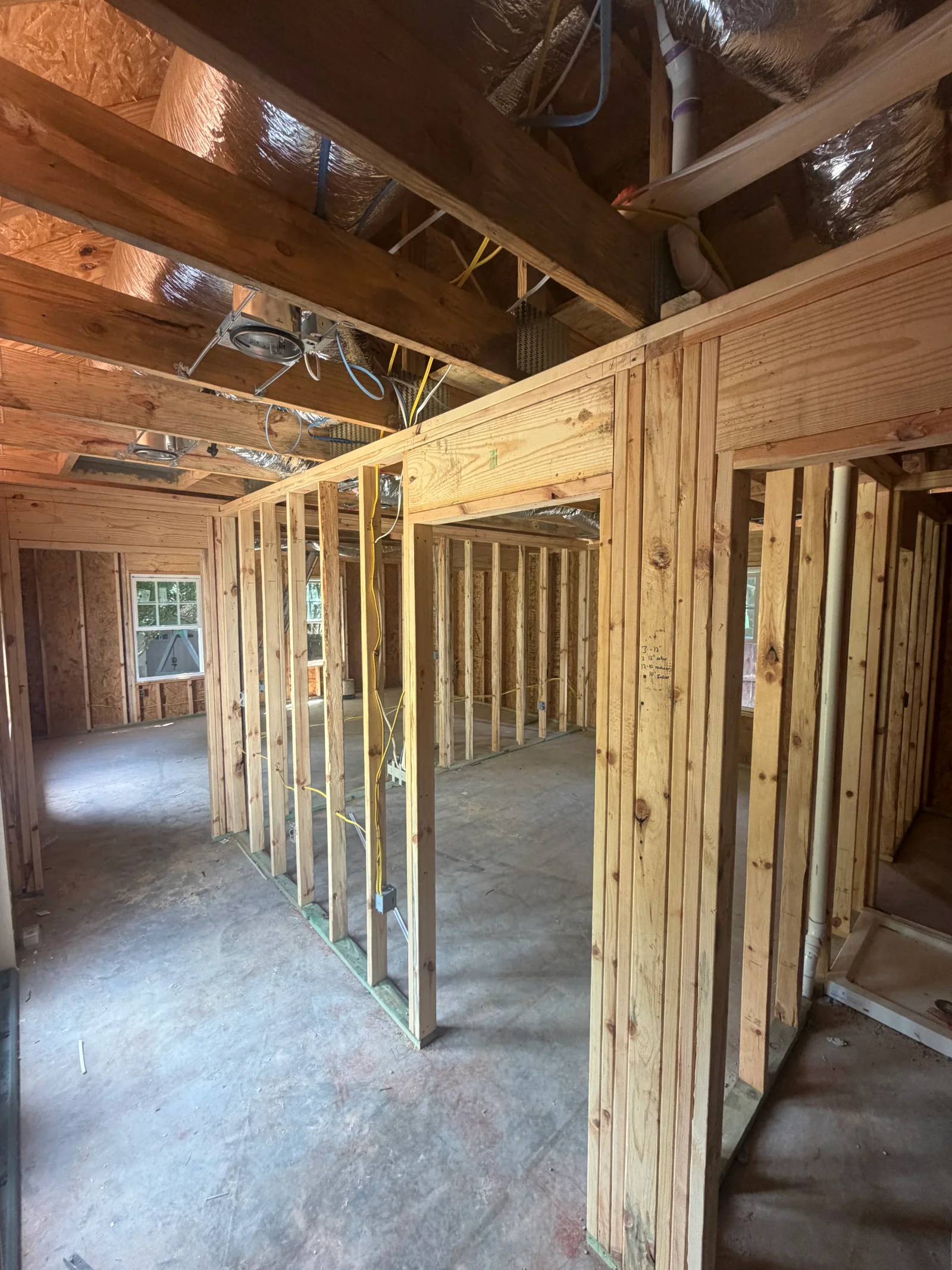 Interior wood-stud wall framing with header, exposed ceiling joists, foil insulation, and rough electrical and PVC plumbing.