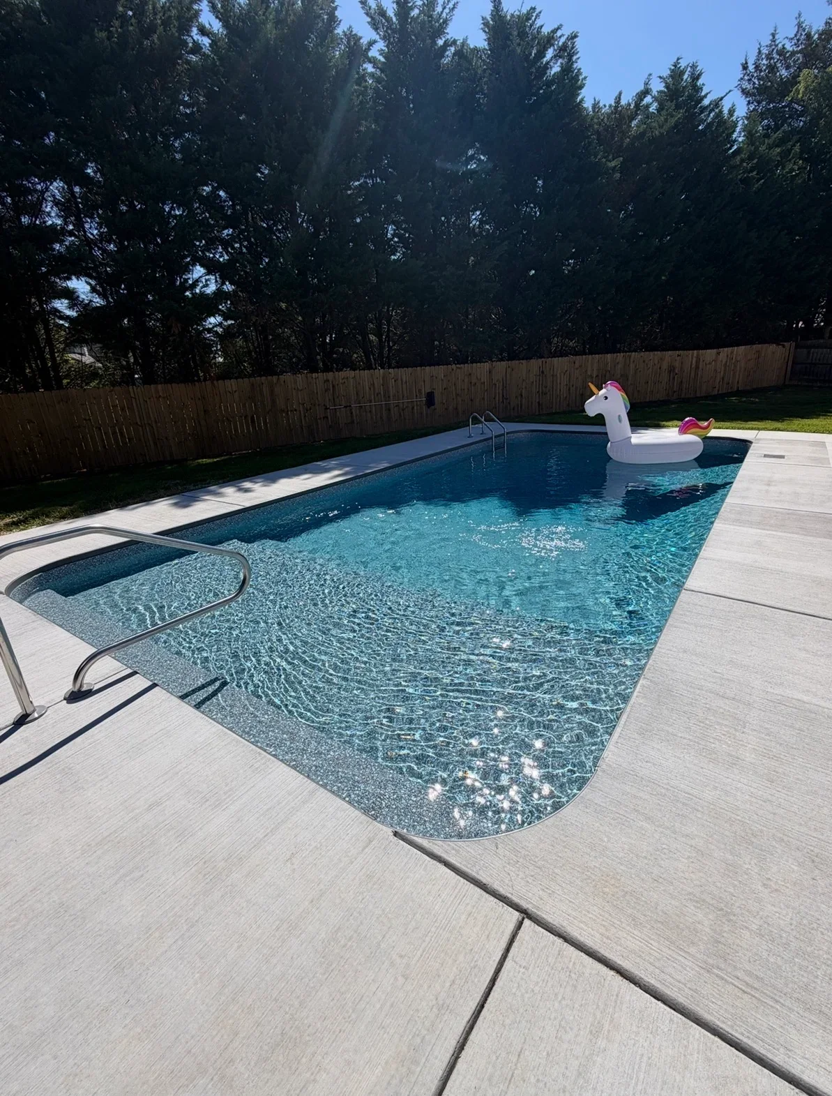 In-ground pool with blue finish, stainless steel handrail, and gray broom-finish concrete decking with saw-cut joints