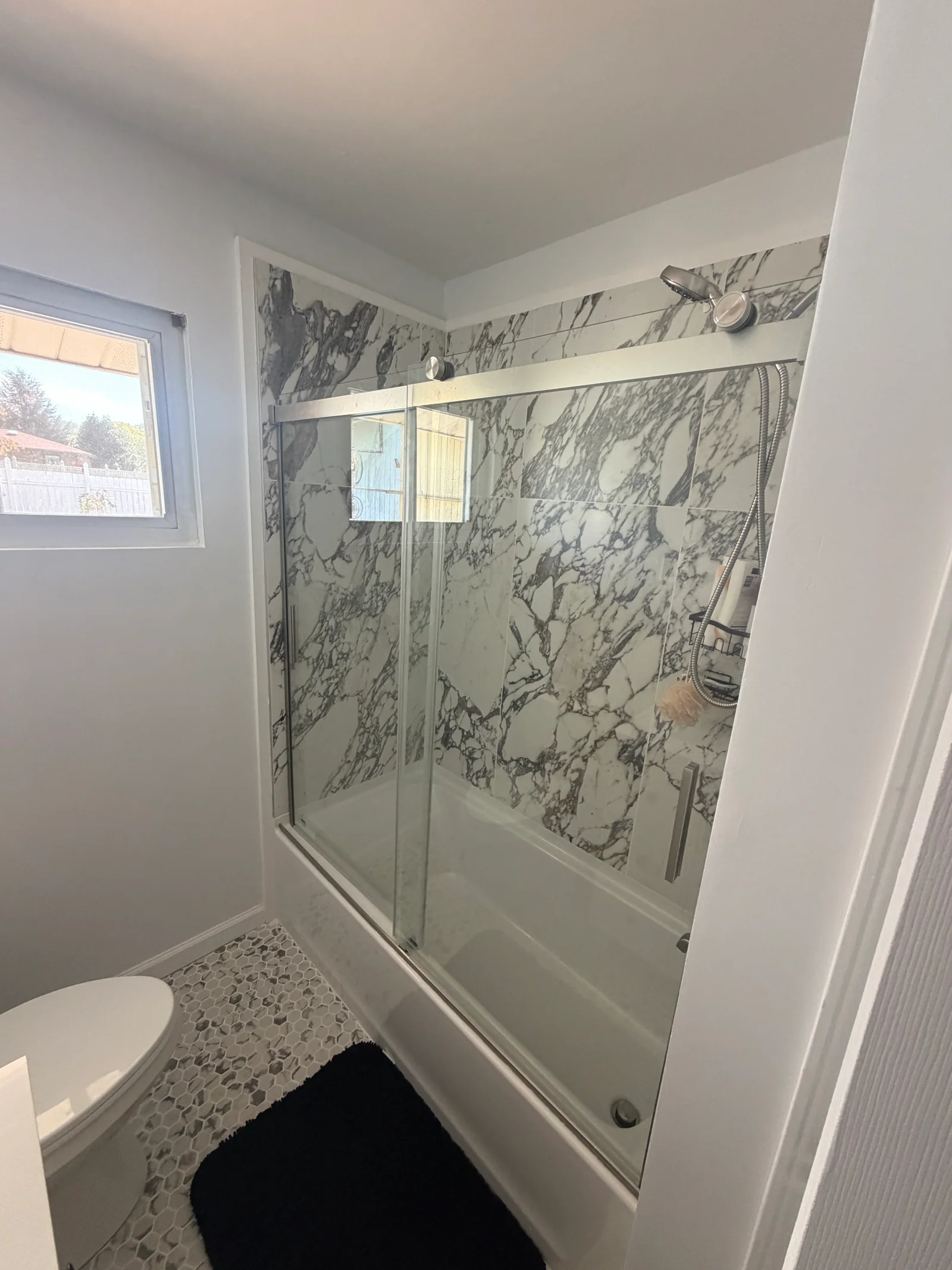 Bathroom tub-shower with large marble-look wall tile, frameless sliding glass door, brushed nickel fixtures, and hexagonal mosaic floor tile