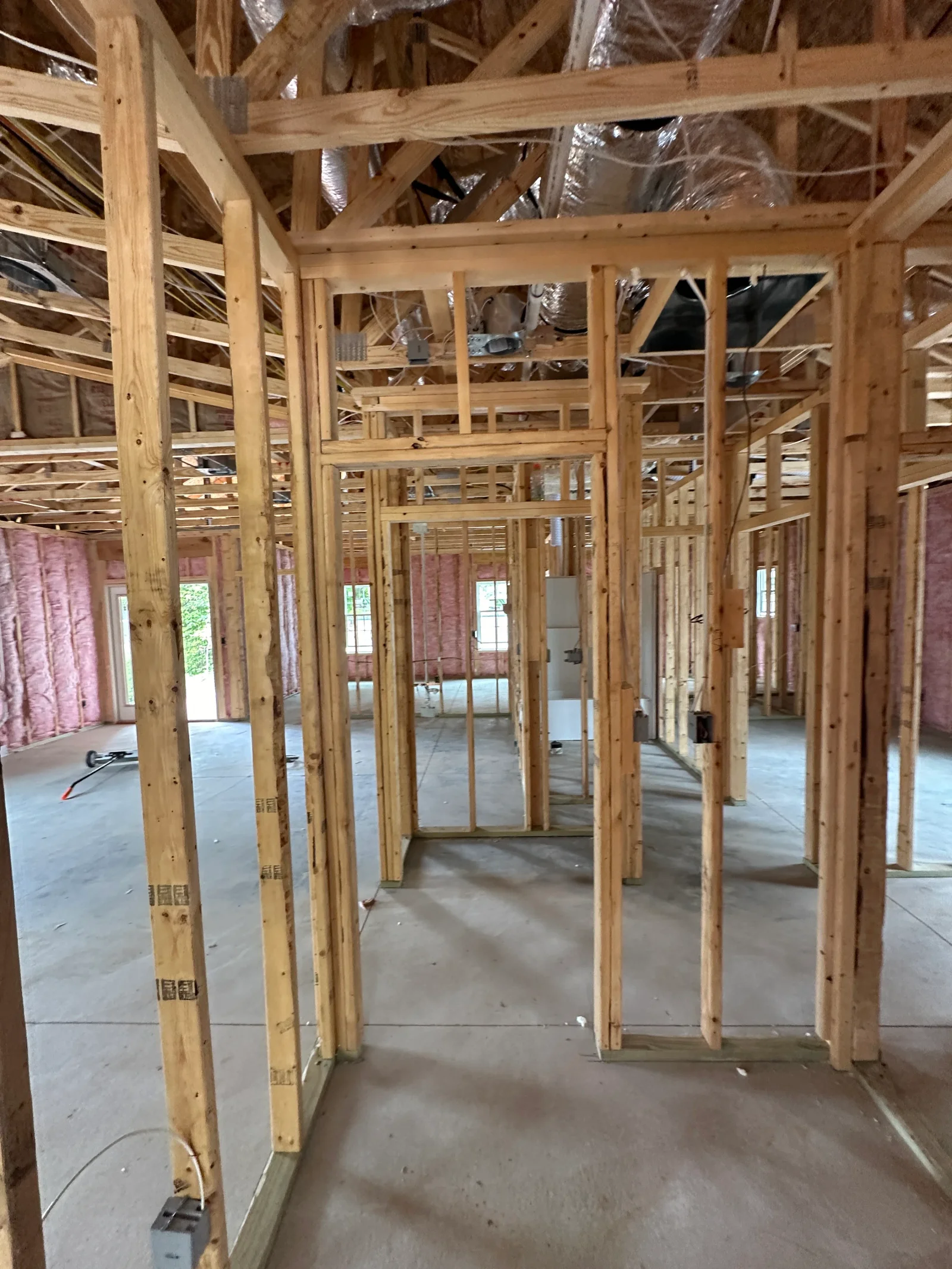 Interior wood stud framing with pink batt insulation, silver flex ductwork, and electrical boxes on concrete slab