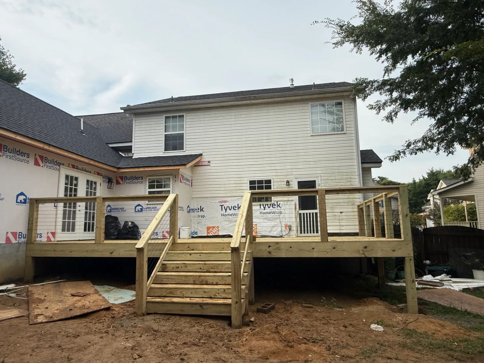 Elevated pressure-treated wood deck with cable railing and wood stairs against a house wrapped in white house wrap